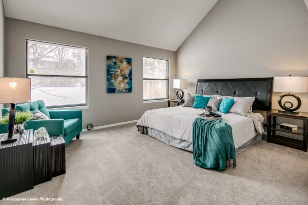 a large transitional master bedroom with gray carpet and teal sofa