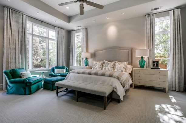 large transitional master bedroom with gray-dominated paintings and teal comfortable sofa