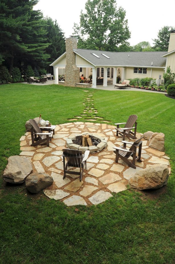 a huge timeless backyard with limestone flagstone paver patio and a fire pit