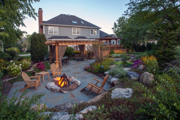 a traditional backyard stone paver patio with a pergola and a fire pit