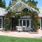 bright attached pergola with flowers to a roof of a gray house