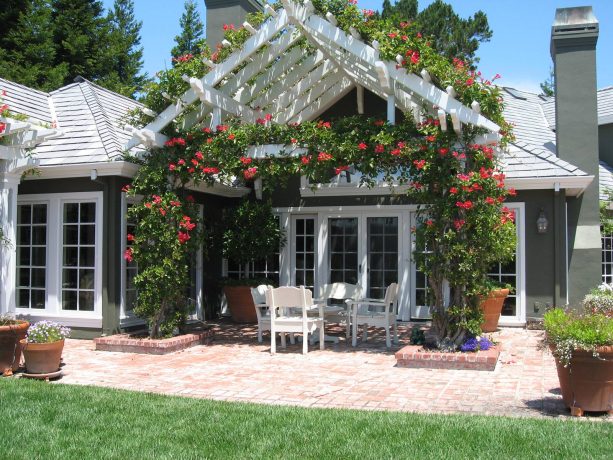 bright attached pergola with flowers to a roof of a gray house