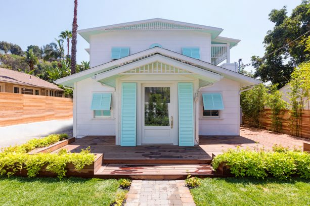 mid-size beach house in white exterior with aquatic blue window & beside door shutters