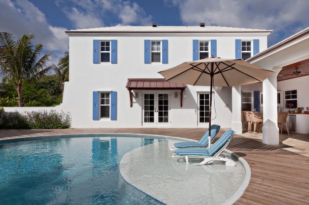 white mediterranean house highlighted by blue shutter, tropical pool & decking