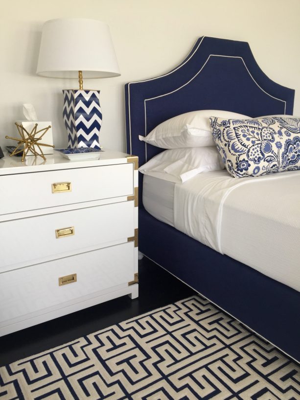navy bed with a white sheet placed against the white wall