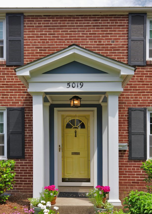 bright yellow front door framed with white posts and surrounded by bricks