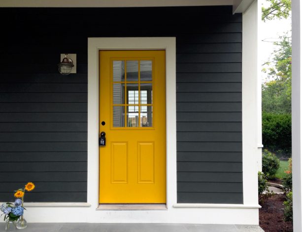 pop of yellow color in a front door around the dark gray siding