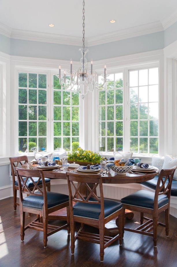 a long bay window with a bench and wooden oval dining table