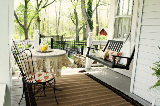 a dark wood swing with two vintage chairs seating on a small front porch