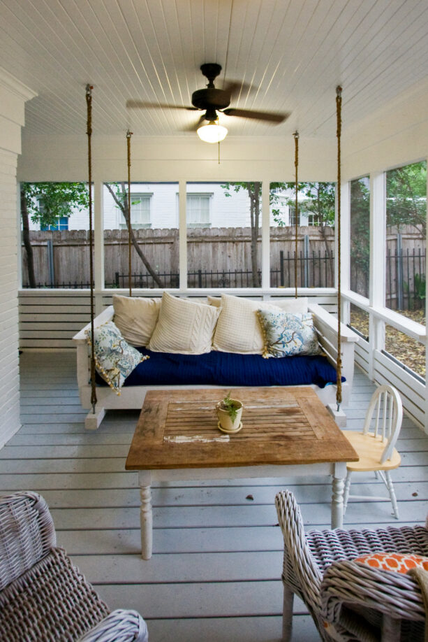 farmhouse front porch with swinging bed, wood, and rattan furniture seating